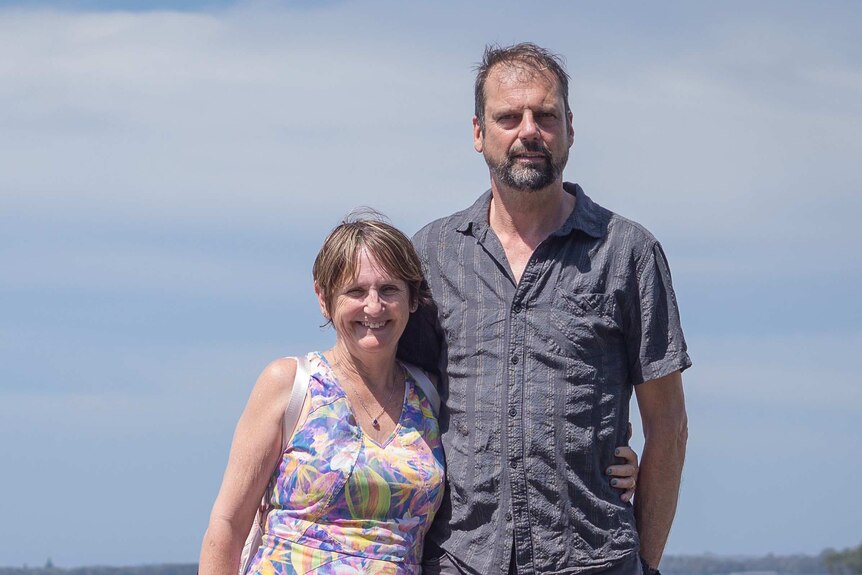 A woman and man stand in front of the ocean, smiling.
