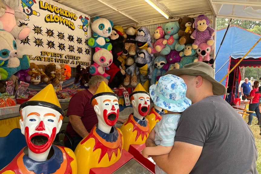 A man holds a small child up to some clown faces