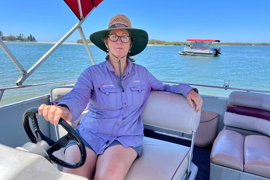 Woman in hat and wearing glasses sitting on a boat.
