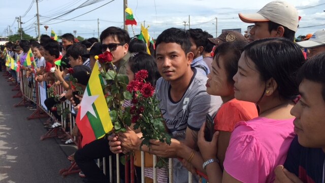 Crowds of Myanmar citizens with flags and flowers gather to greet Aung San Suu Kyi at a seafood market south of Bangkok.