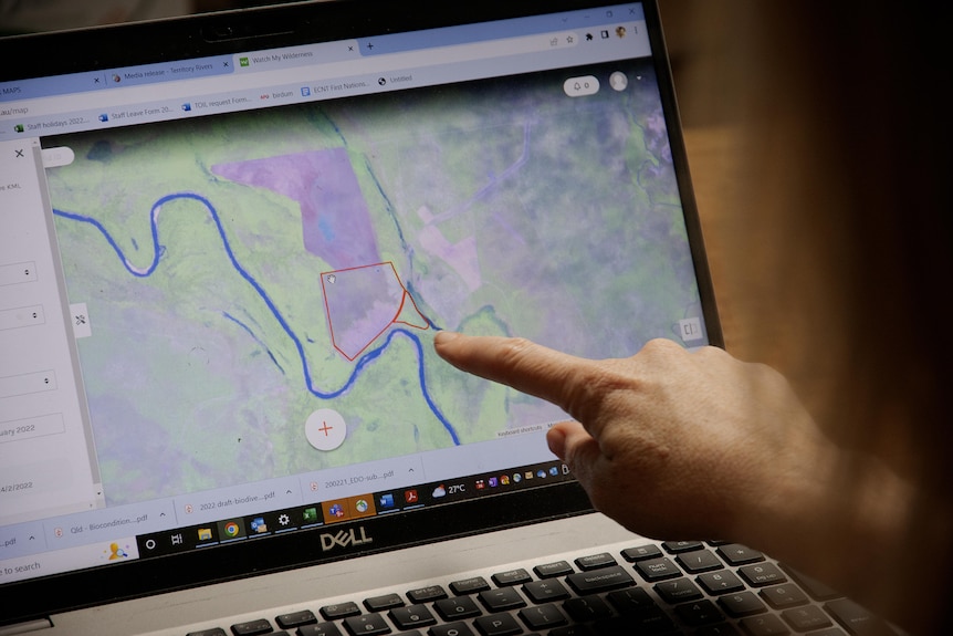 Satellite imagery of land clearing on a computer screen with an index finger pointing.