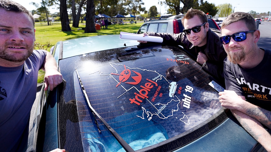Three punters from Brisbane stand next to a sticker on their car's rear window documenting their four day journey to Lucindale.