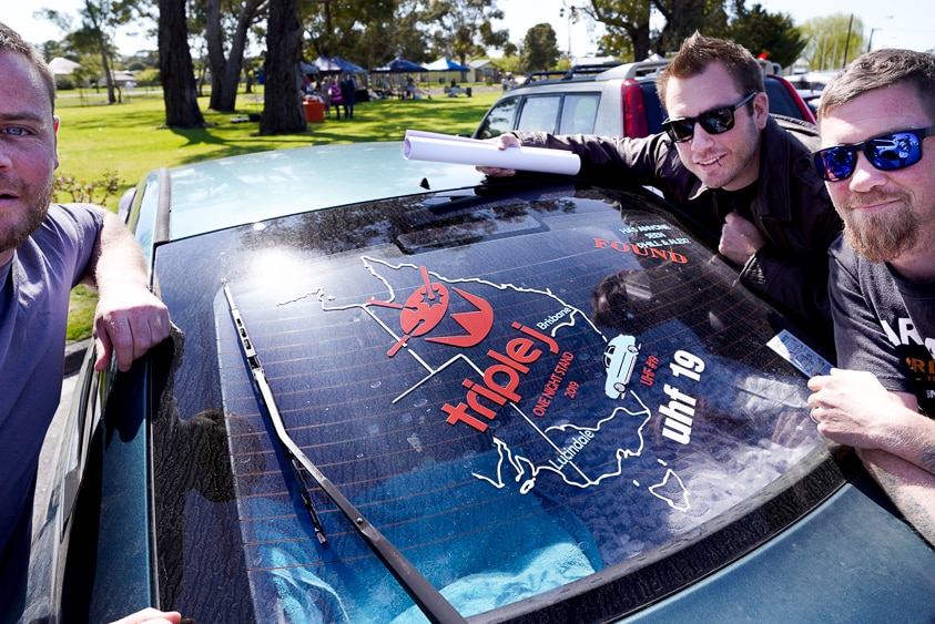 Three punters from Brisbane stand next to a sticker on their car's rear window documenting their four day journey to Lucindale.