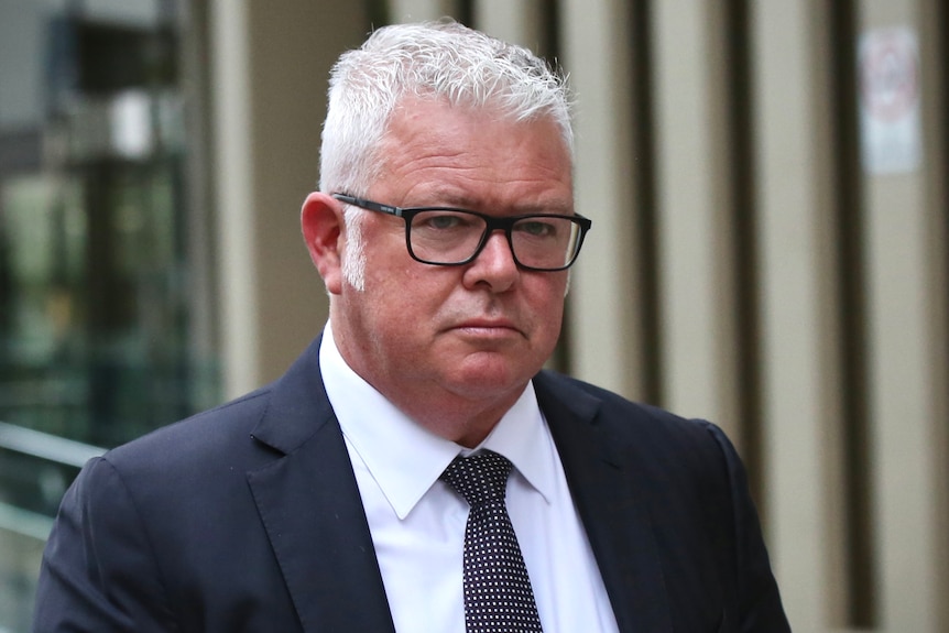 A head and shoulders shot of a stern looking Troy Buswell outside court wearing a suit and tie.