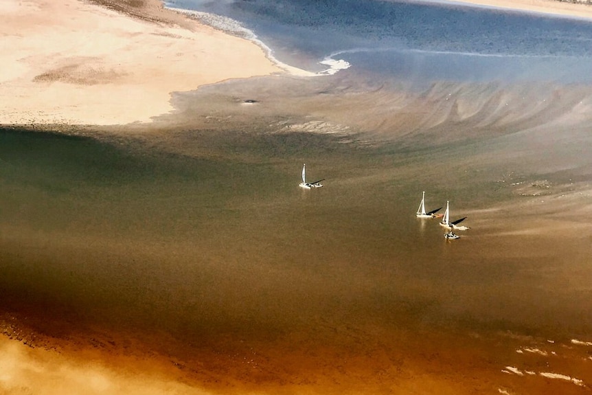An aerial view of white boats floating on a lake in the desert. 