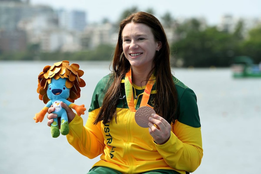 Susan Seipel in Aussie green and gold. In one hand her bronze medal, in the other a stuffed toy mascot. 