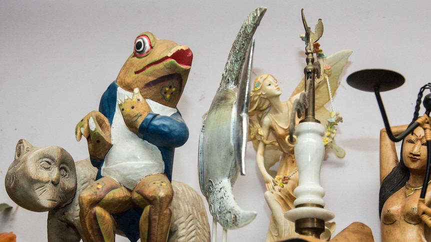 A wooden figurine of a frog sits alongside other ornaments on a shelf.