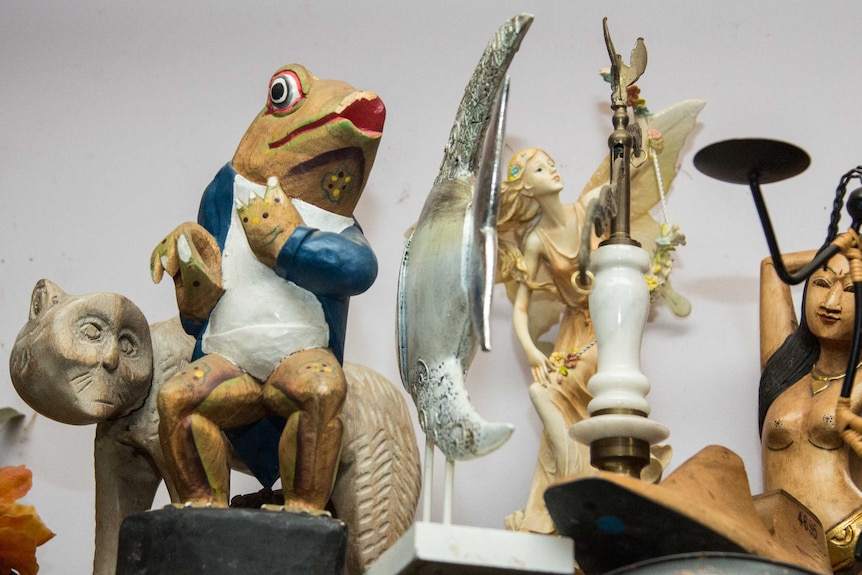 A wooden figurine of a frog sits alongside other ornaments on a shelf.