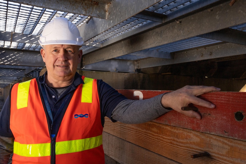 A man in high vis and hard hat stand under a walking platform 