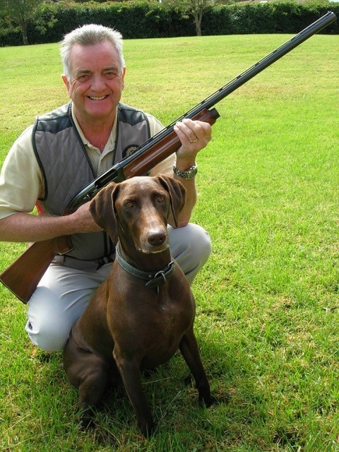 A man holding a shotgun with a dog. 