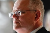 A close shot of a man with grey hair and glasses wearing a suit and tie looking to the left