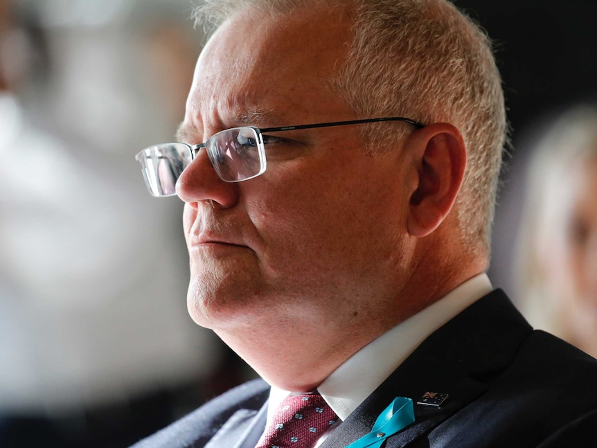 A close shot of a man with grey hair and glasses wearing a suit and tie looking to the left