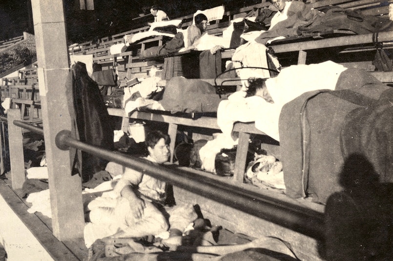 A black and white image of young men sleeping on seats in a grandstand.