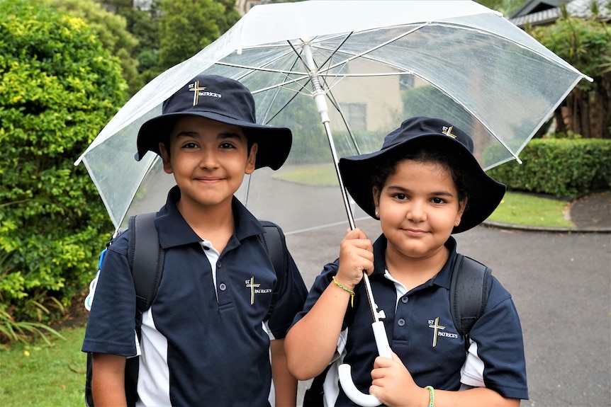 A syrian boy and his sister in school uniform holding a see-through umbrella.
