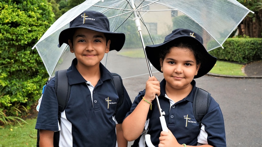 A syrian boy and his sister in school uniform holding a see-through umbrella.