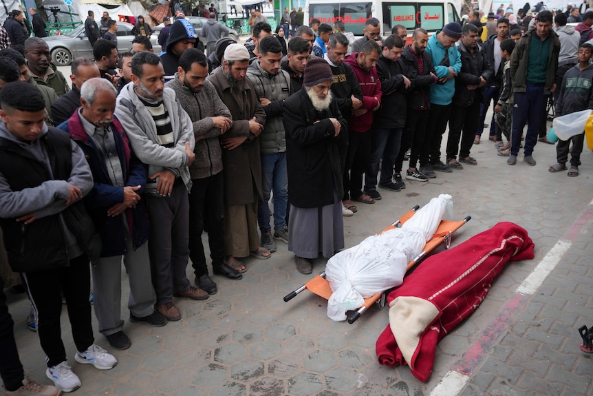 Un gruppo di persone in piedi accanto a due corpi avvolti in una strada cittadina