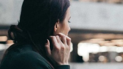 Woman leans on balcony with head on hand, blurred background with people