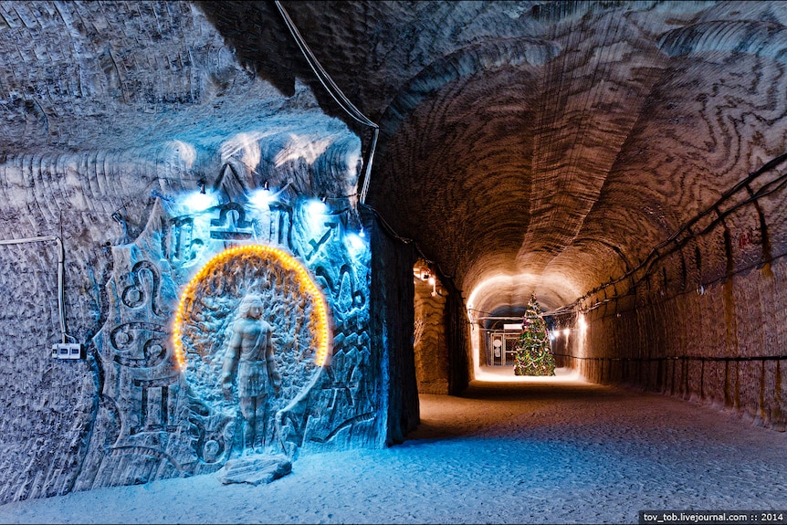 A sculpture of a figure surrounded by symbols is illuminated on the wall of a salt mine.