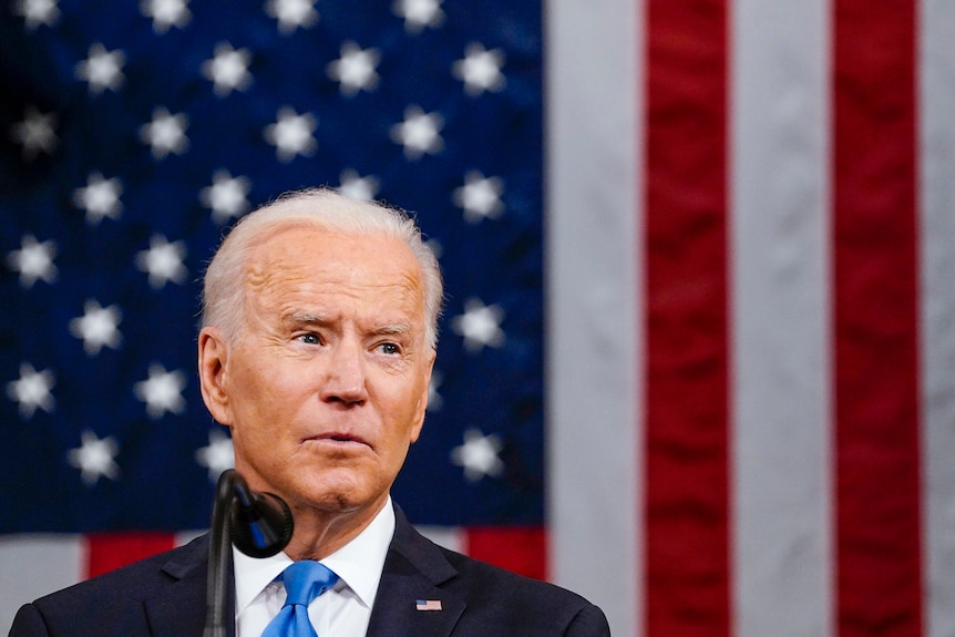 Joe Biden parla al microfono davanti a una bandiera americana