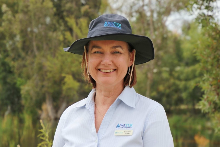 A woman in a navy blue hat and light blue shirt poses for a photo at a park