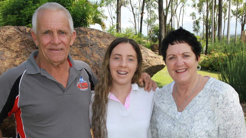 Father, daughter and mother stand in front of a rock formation in a lush garden.