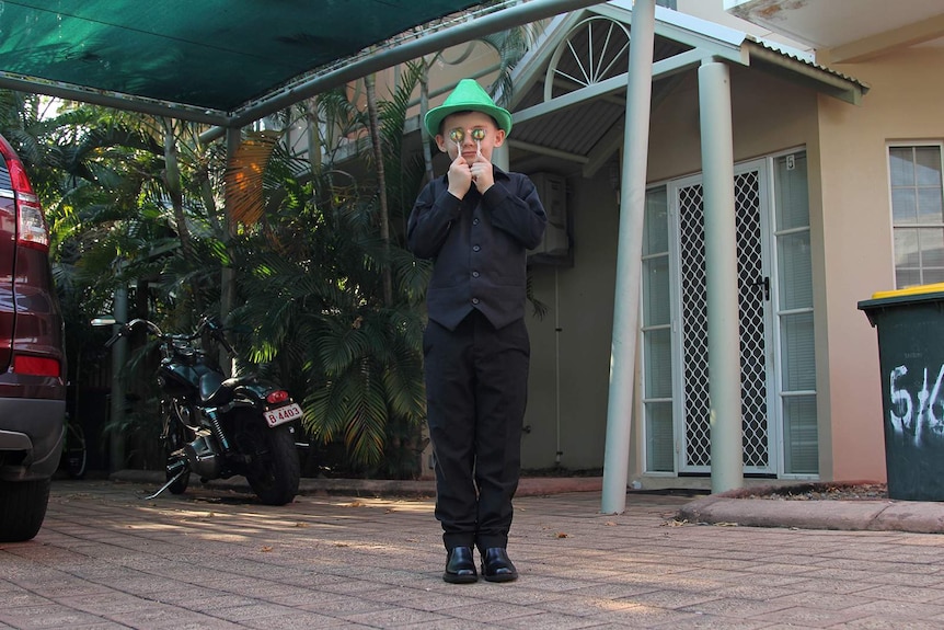 A photo of eight-year-old Angus Copelin-Walters standing in front of his apartment with two lollipops in front of his eyes.