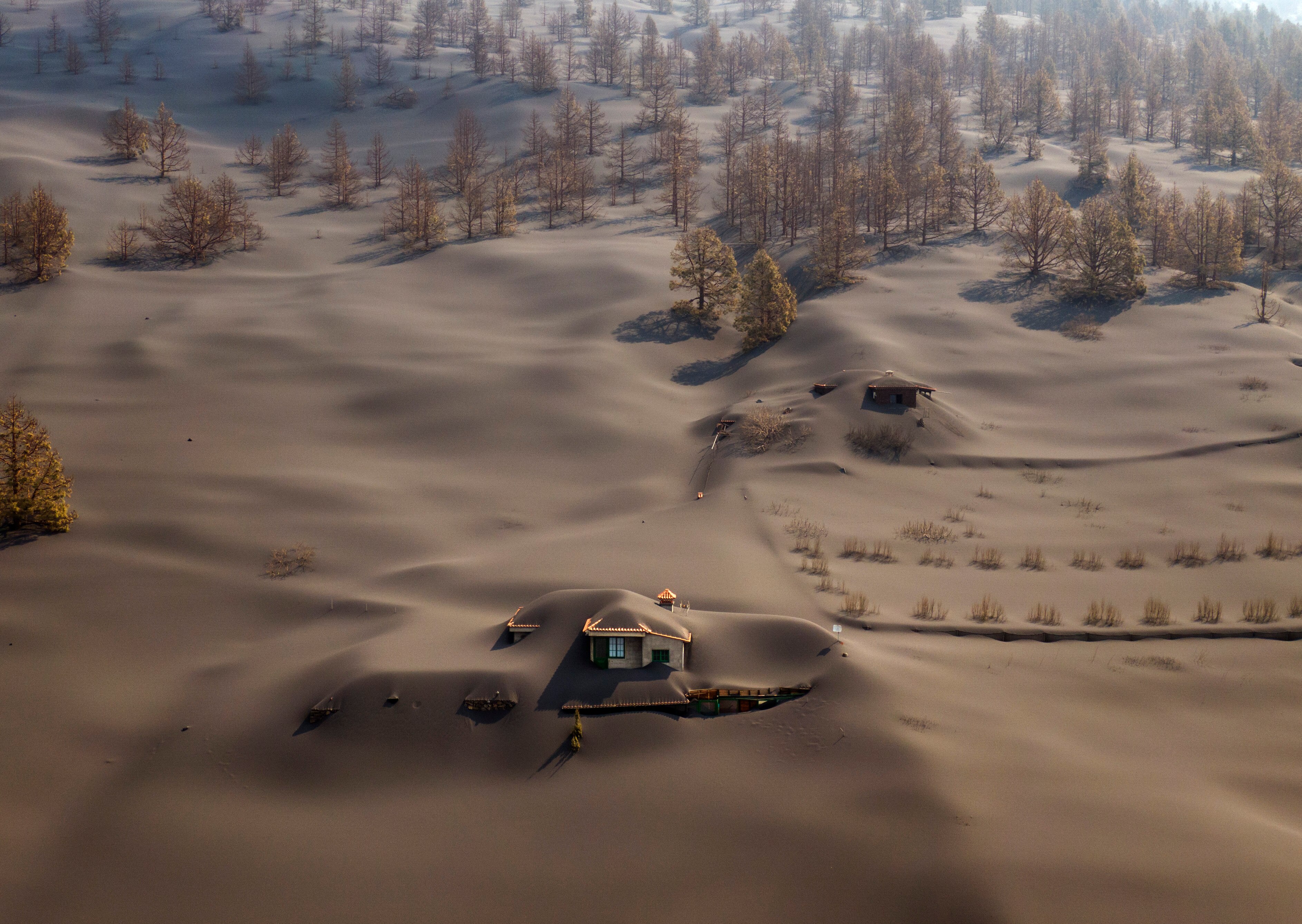 A vast ground covered in ash with remnants of a house visible