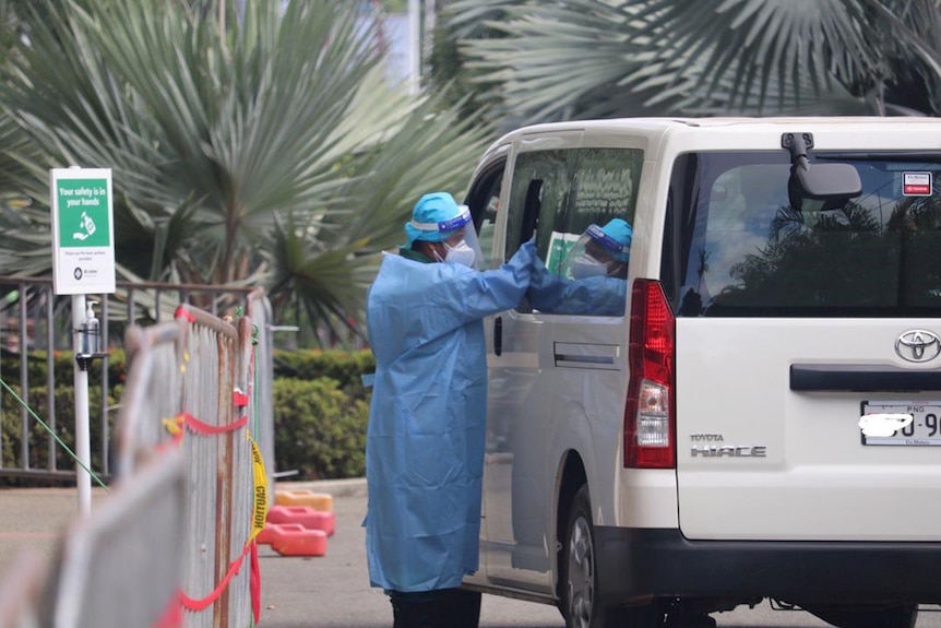 A person in full PPE leans into the window of a van.