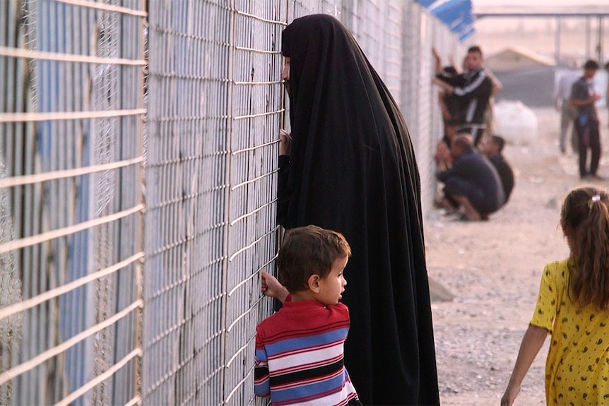 A woman and children look through bars of a special security area at the Debaga camp in North Iraq.