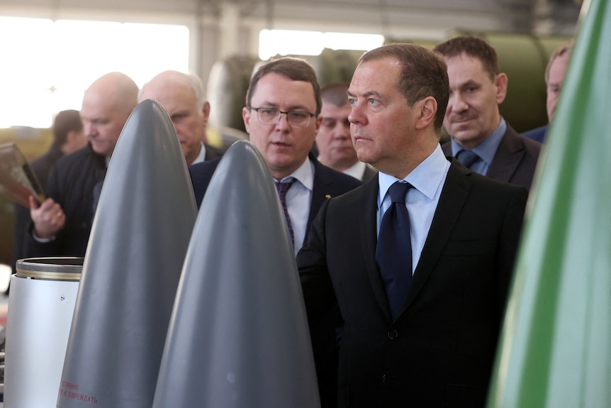 Dmitry Medvedev inspects missiles, flanked by officials.