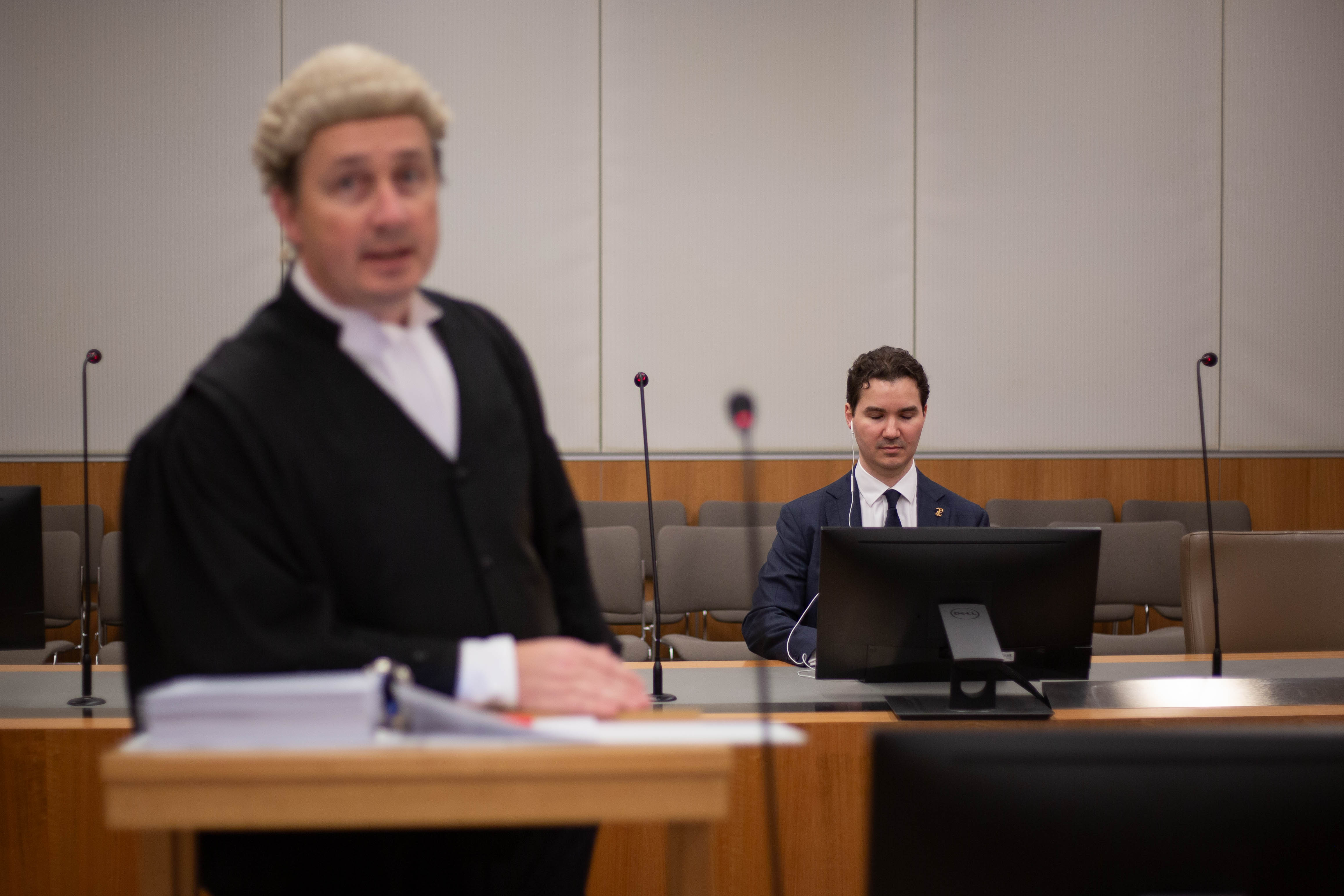 A barrister in a court room standing at a bench in front of a man at his laptop
