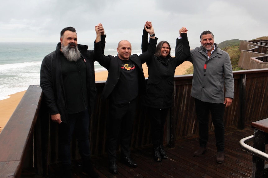 indigenous leaders holding hands on viewing platform to ocean behind