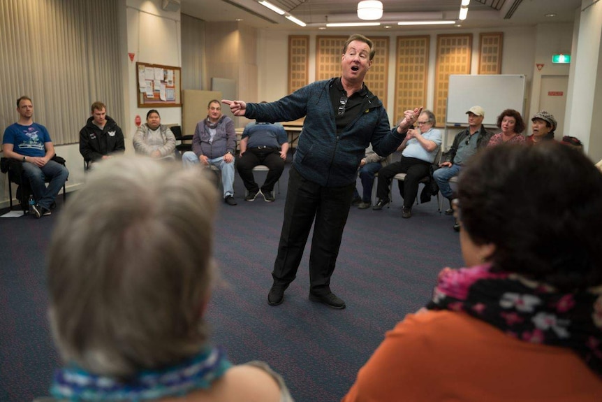 A choir master leads a group in singing as they sit in a circle