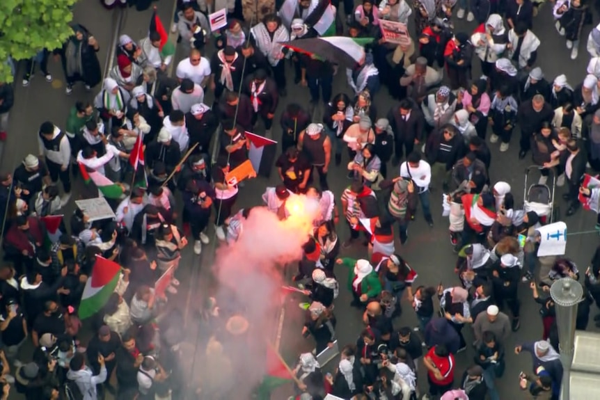 An aerial shot of a crowd of protestors, with people appearing to let off a flare.