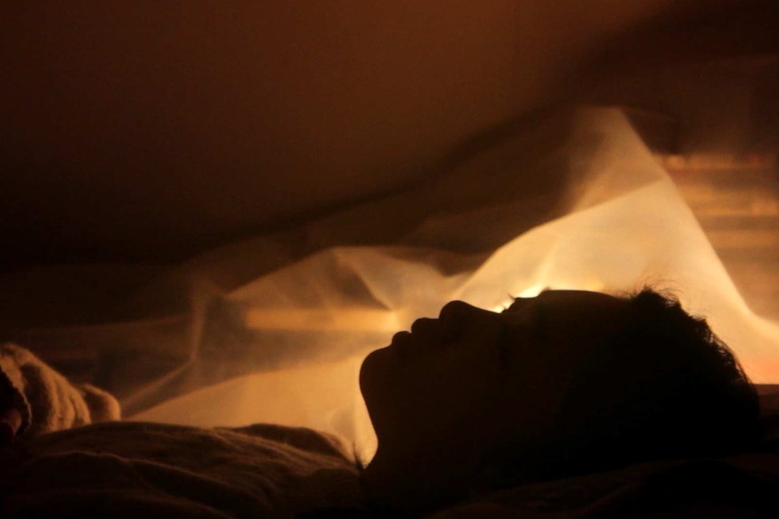 A woman lies in bed looking thoughtfully up at the ceiling.