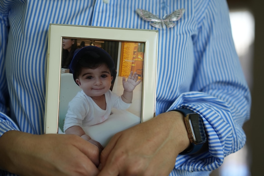 A woman holds a photo of a toddler.