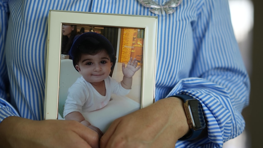 A woman holds a photo of a toddler.