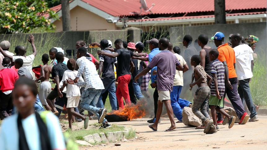 Men and boys run away as a tyre is set on fire.