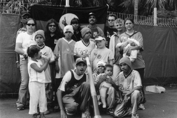 Photo of the Wilcannia Mob standing in front of an aboriginal flag at Homebake in 2002.