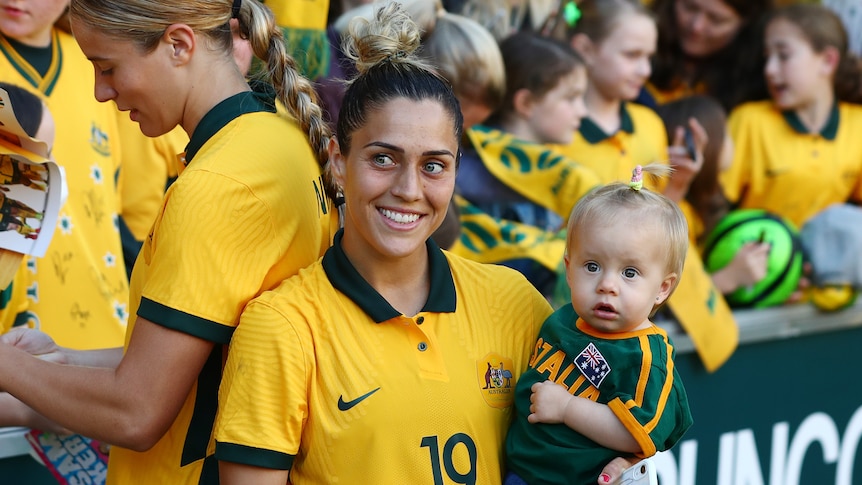 A footballer smiles while holding her baby daughter.