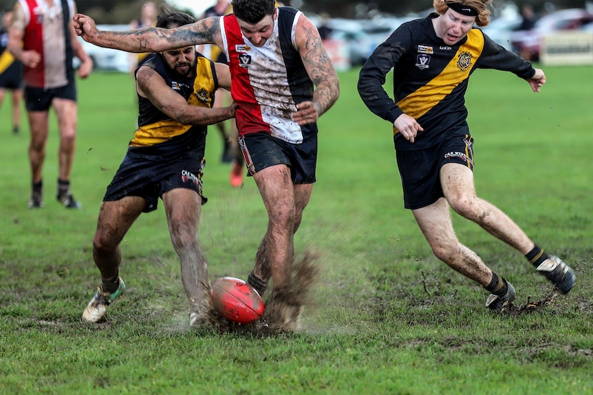 Muddy water splashes off football ground as players chase ball on green grass