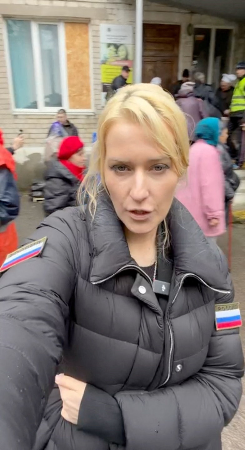 A blonde woman in grey winter jacket with Russian flags on her arms