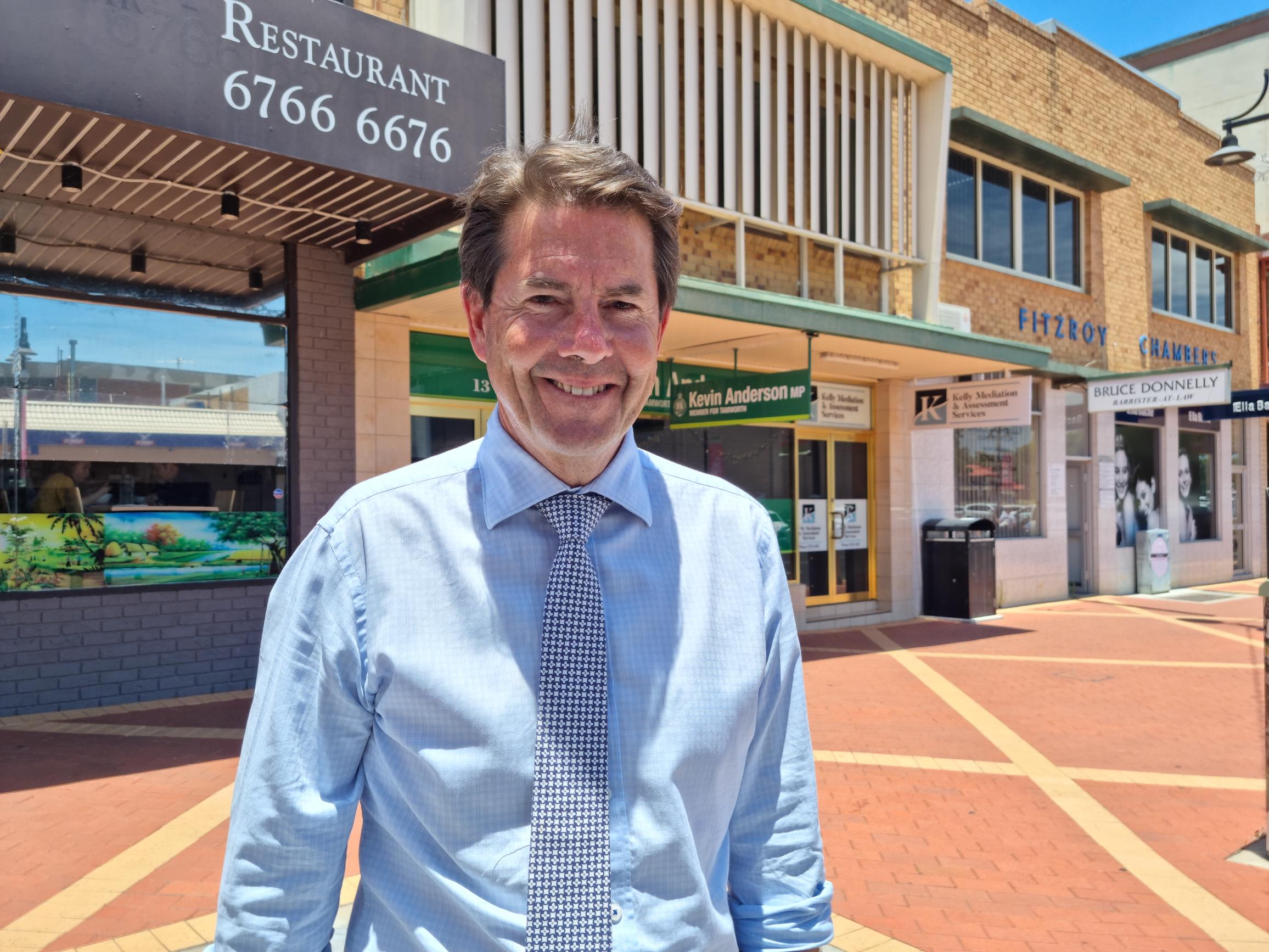 A man standing in front of a shopfront in a shopping plaza.