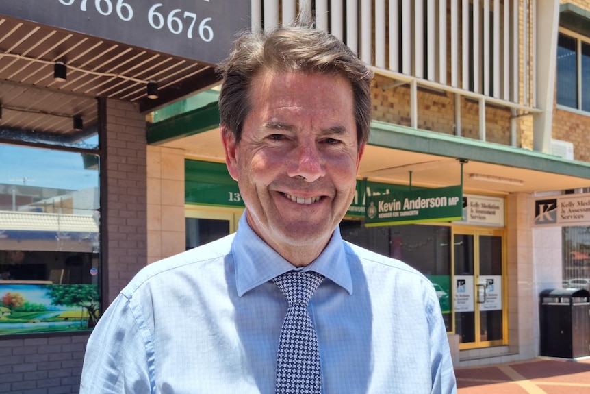 A man standing in front of a shopfront in a shopping plaza.