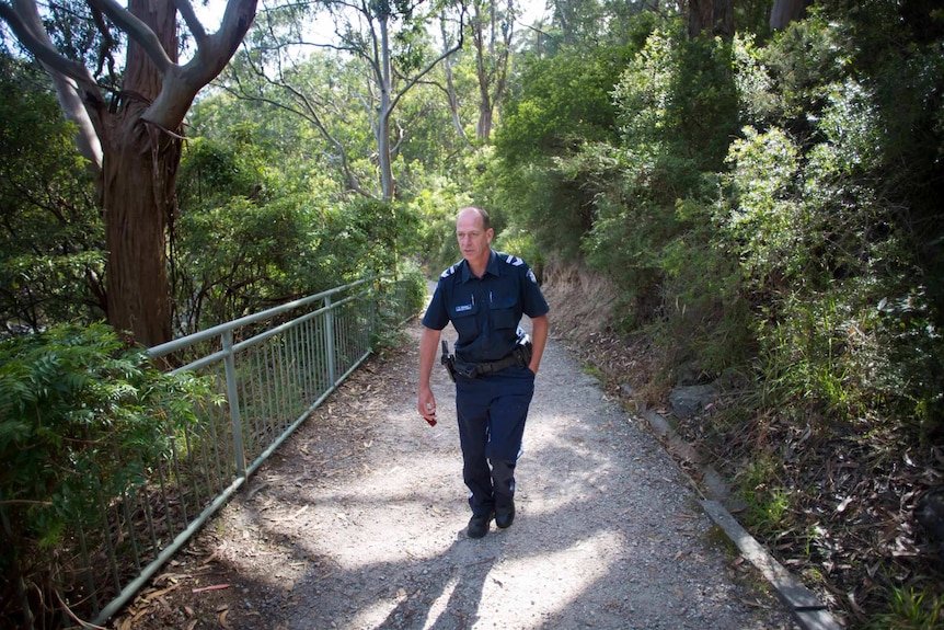 Policeman Paul Delaney walks up a track surrounded by bush.