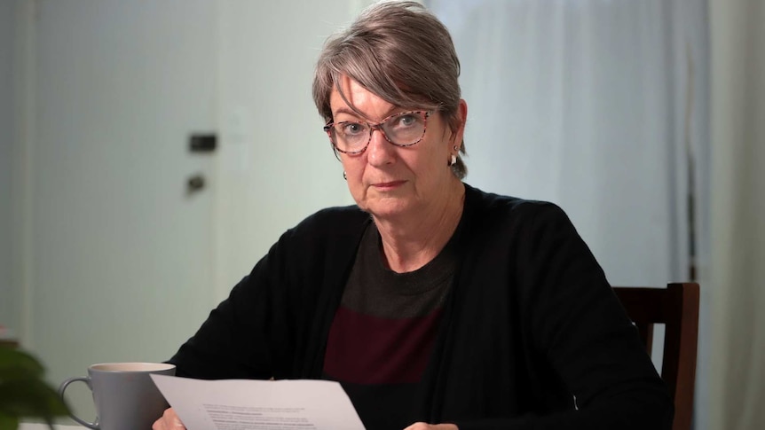 Pamela Robertson sitting at a table holding a letter.