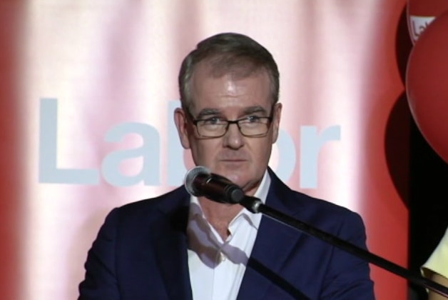 man on stage with red Labor signs behind him