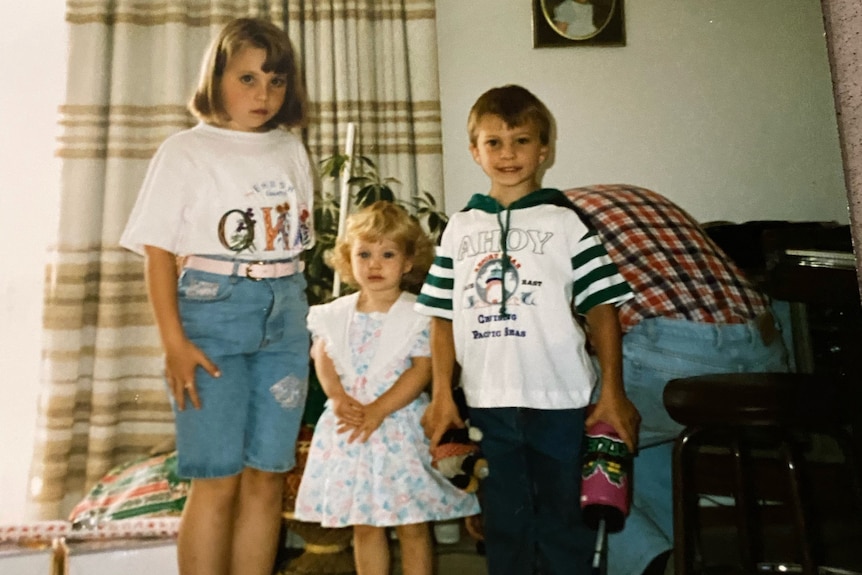 Three children stand in a line and pose for a photo.