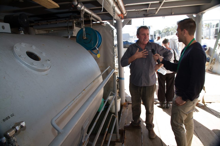 A man standing next a decompression chamber aboard a warship speaks to a reporter.