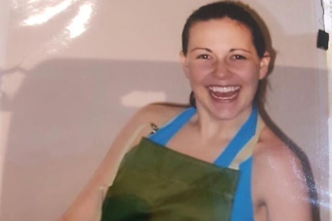 A smiling young woman sits on a couch in a house wearing an apron.